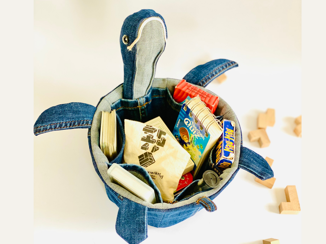 Jeans-Utensilo in Schildkrötenform mit Innentaschen, gefüllt mit Spielzeug und Karten