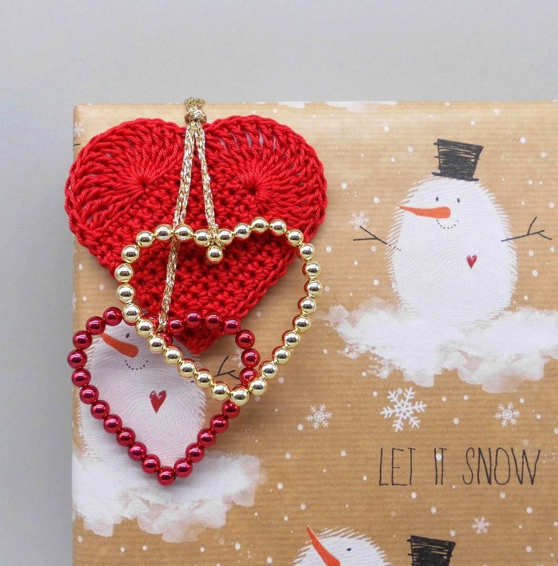 Red crocheted heart with gold and red beaded heart outlines tied on snowman-patterned gift wrap.