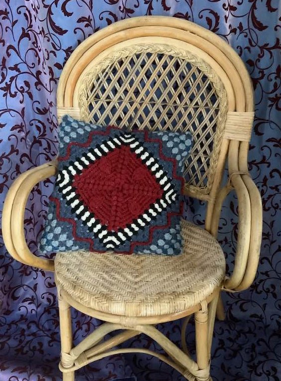 Gehäkeltes quadratisches Dekokissen mit roter Raute und schwarz-weißen Zickzacklinien auf einem Rattanstuhl