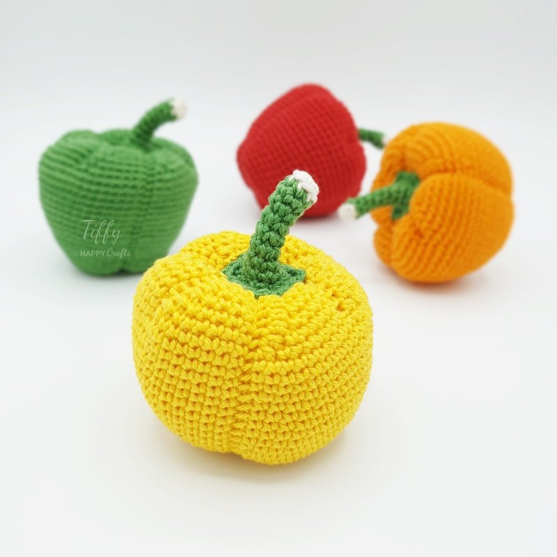 Four brightly colored crocheted bell peppers, yellow, green, red, and orange.