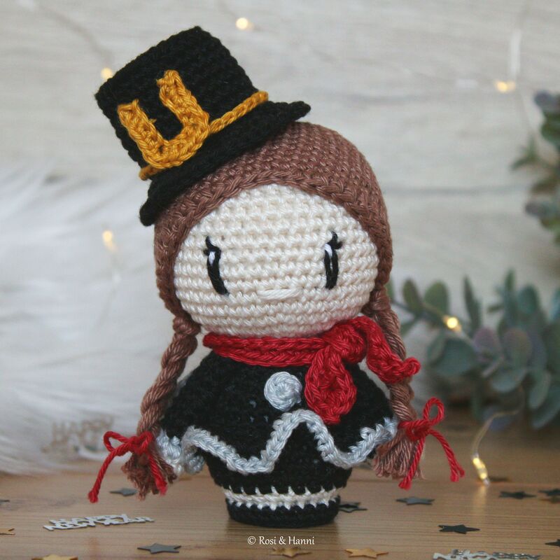 Gehäkelte Amigurumi-Puppe mit Zylinderhut, rotem Schal und geflochtenen Zöpfen vor Lichterkette
