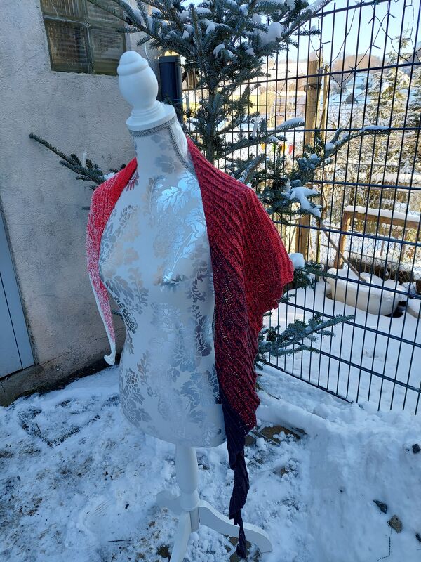 Gehäkeltes halbrundes Tuch in Rot und Schwarz auf einer Schneiderpuppe im Schnee.