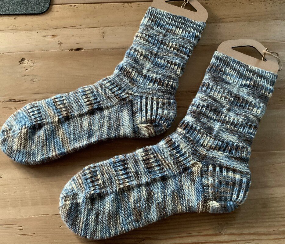 Handgestrickte Socken mit blau-braunem Melange-Muster auf Holzuntergrund.