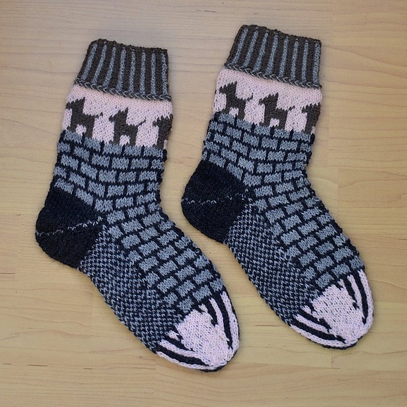 Paar gestrickter Socken in Rosa und Grau mit Hundemotiv und Ziegelmuster