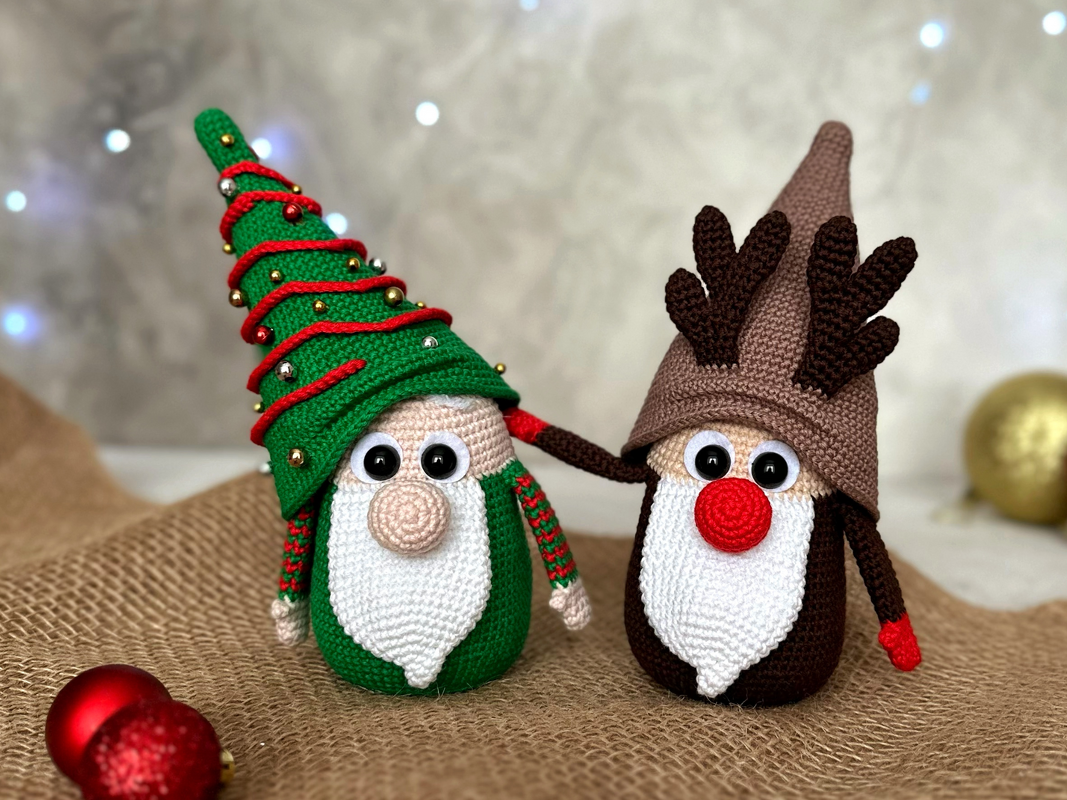 Zwei gehäkelte Weihnachtswichtel, einer im Baum‑Design, der andere als Rentier, auf Jutestoff.