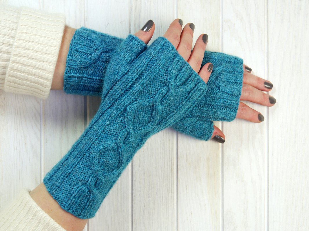 Teal cable knit fingerless gloves on hands showing textured cable pattern and open fingertips.