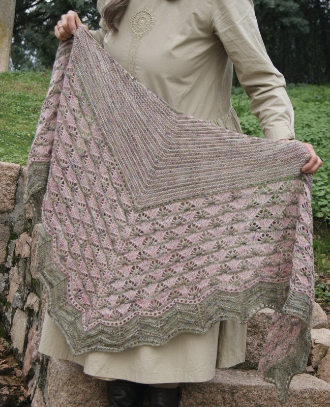 Gestricktes Dreieckstuch in Rosa und Grün mit Fächermuster, gehalten von einer Person im Freien.