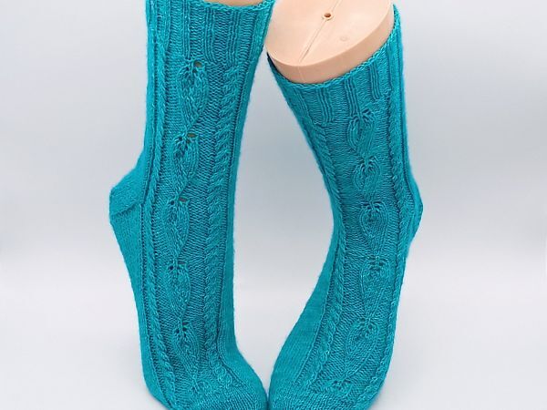 Türkise gestrickte Socken mit Zopf- und Blatt-Ajourmuster auf Modellfüßen
