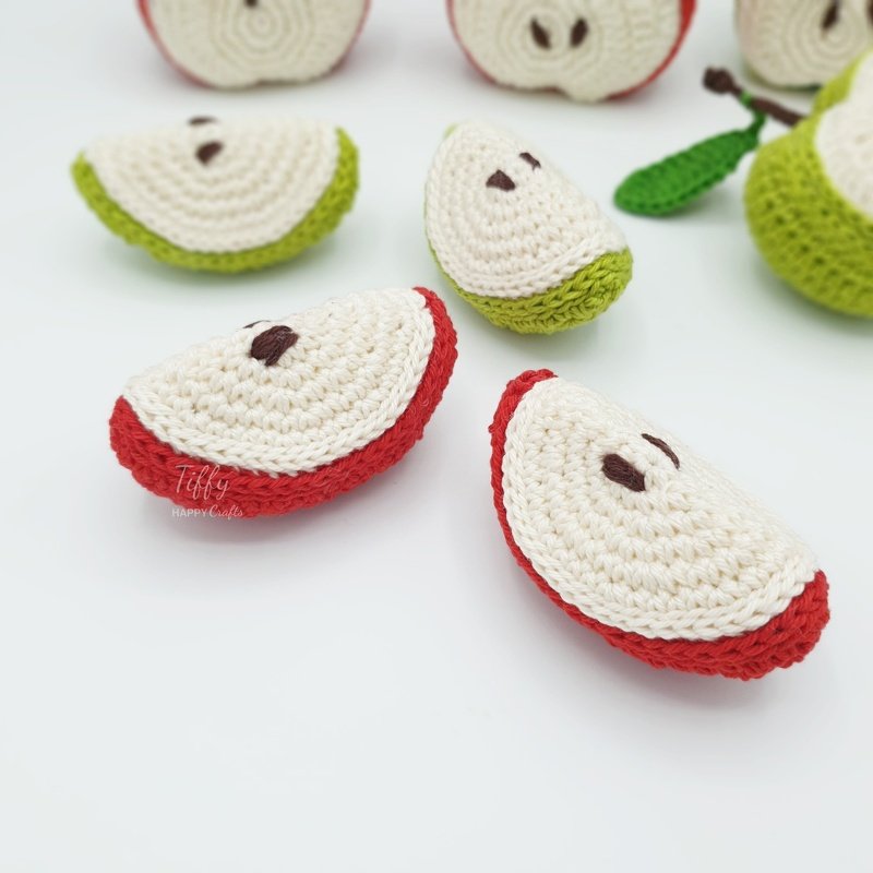 Hand-crocheted red and green apple slices on white surface