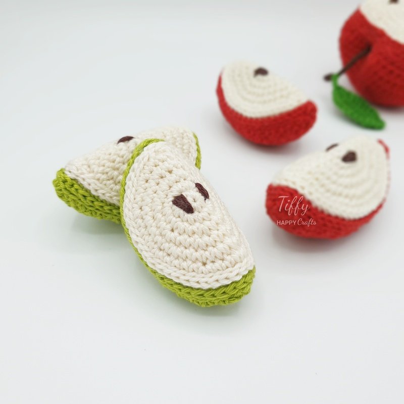 Red- and green-edged crocheted apple slices with a whole red crocheted apple on a white background.