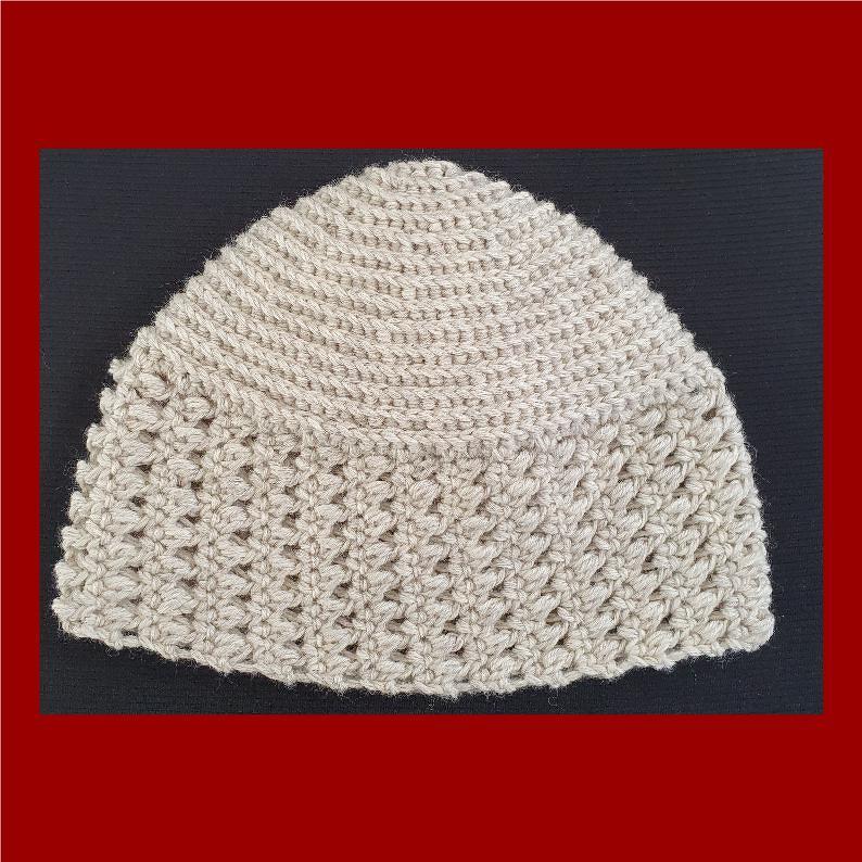 Hellbeige gehäkelte Beanie mit strukturiertem Rand vor dunklem Hintergrund