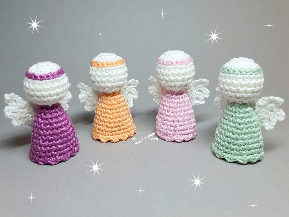 Vier gehäkelte Amigurumi-Engel in Lila, Orange, Rosa und Mintgrün mit weißen Köpfen und Flügeln auf grauem Hintergrund.