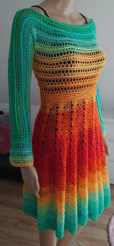 Nahaufnahme eines gehäkelten Damenkleides in Türkis, Gelb, Orange und Rot mit langen Ärmeln, breitem Ausschnitt und A‑Linien‑Rock auf einer Schaufensterpuppe.