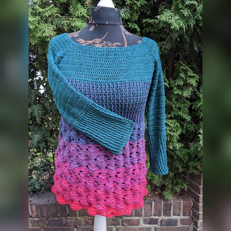 Gehäkelte Tunika in Türkis–Lila–Pink mit offenem Muschelsaum auf Schneiderpuppe