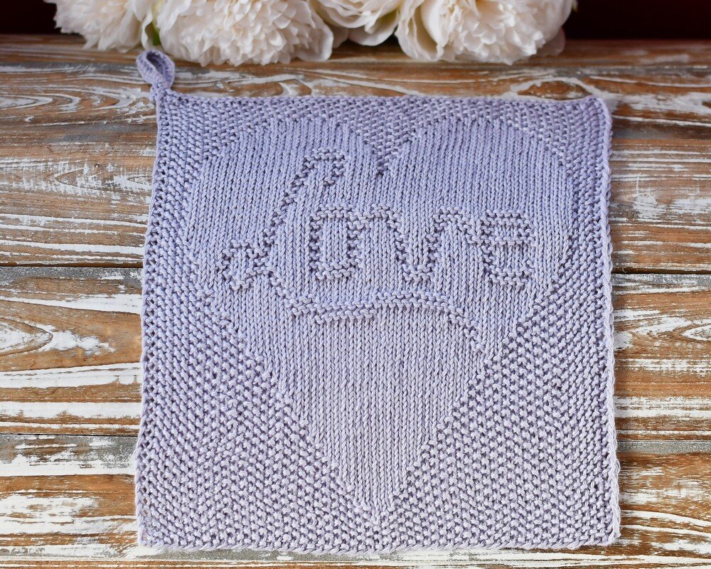 Gestricktes quadratisches Tuch in lila mit Herz- und LOVE-Muster auf Holzuntergrund.