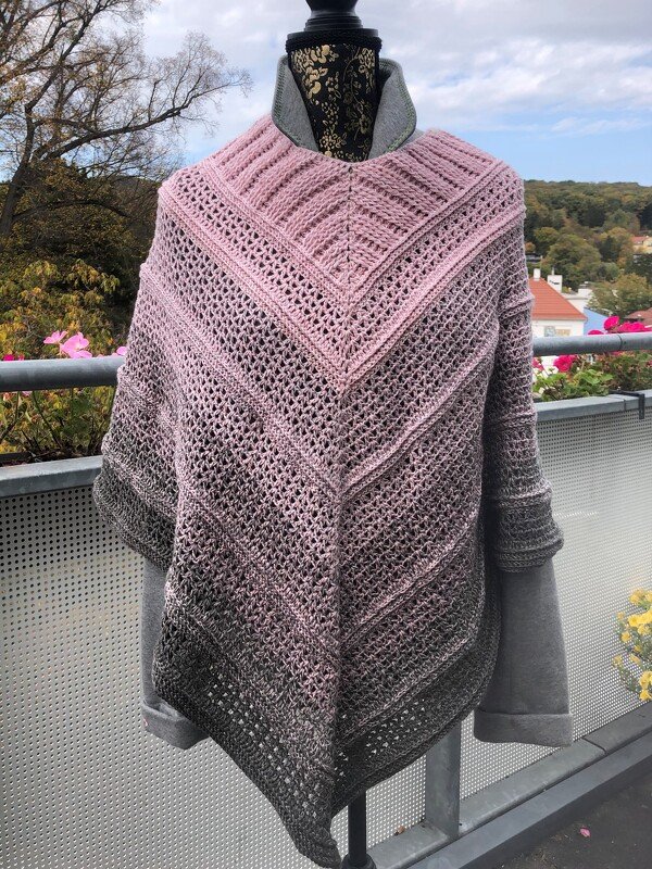 Gehäkelter Damenponcho in Rosa und Grau mit Ombré-Farbverlauf und V-Form auf einem Mannequin im Freien