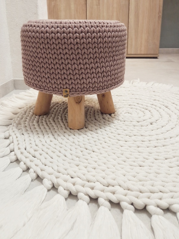 Gehäkelter Pouf mit Holzfüßen auf rundem Häkelteppich mit Quasten