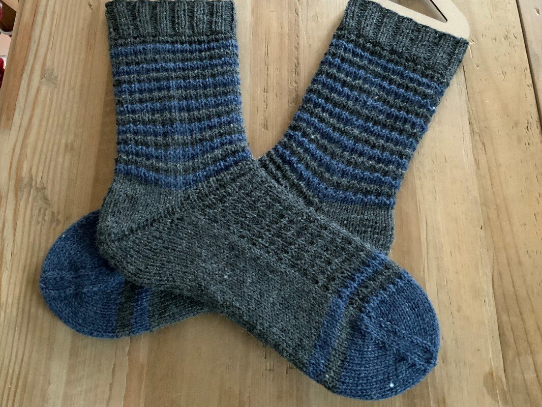 Gestrickte dunkelgraue Socken mit blauen Streifen auf Holz