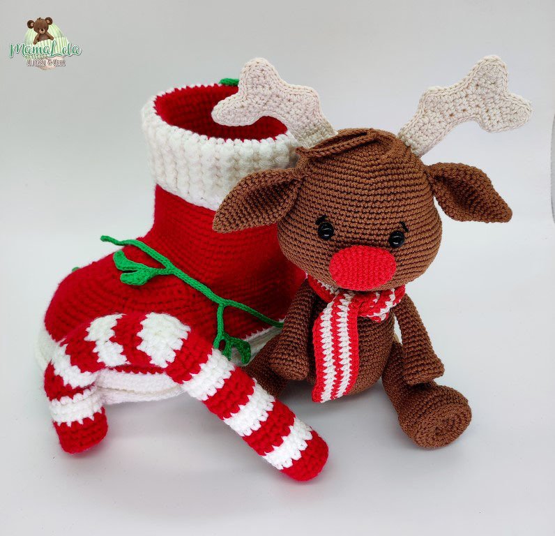 Gehäkeltes Amigurumi-Rentier mit roter Nase und rot-weißem Schal neben Nikolausstiefel und rot-weiß gestreifter Zuckerstange.