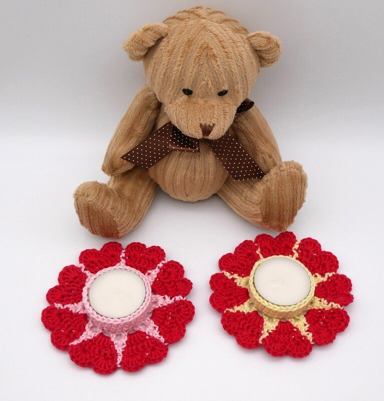 Zwei gehäkelte Herz-Untersetzer mit Teelichtern und Teddybär im Hintergrund