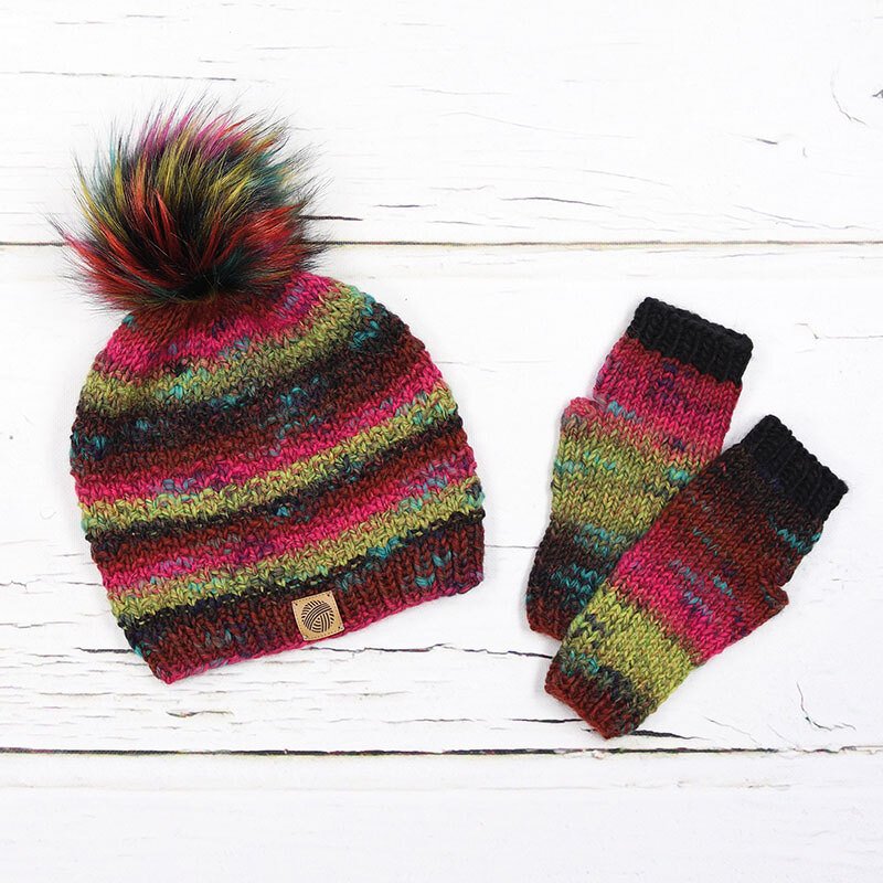 Bunt gestreifte Strickmütze mit Bommel und fingerlose Strickhandschuhe auf weißem Holzuntergrund