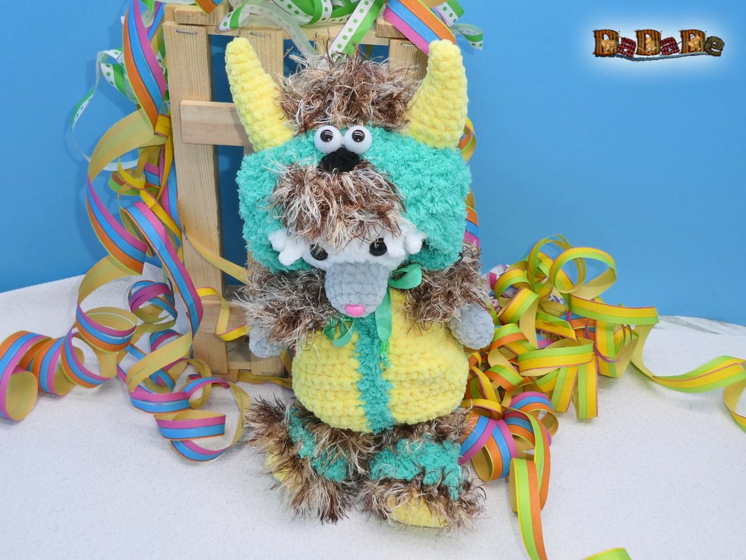 Gehäkeltes Amigurumi im gelb-türkisen Monsterkostüm mit gelben Hörnern und bunten Luftschlangen