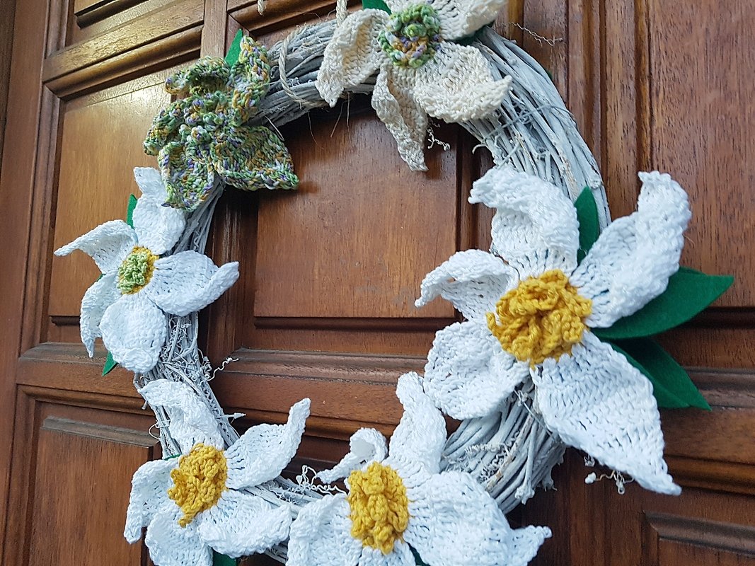 Gehäkelter Türkranz mit weißen Blüten mit gelben Details und grünen Blättern an einer Holztür