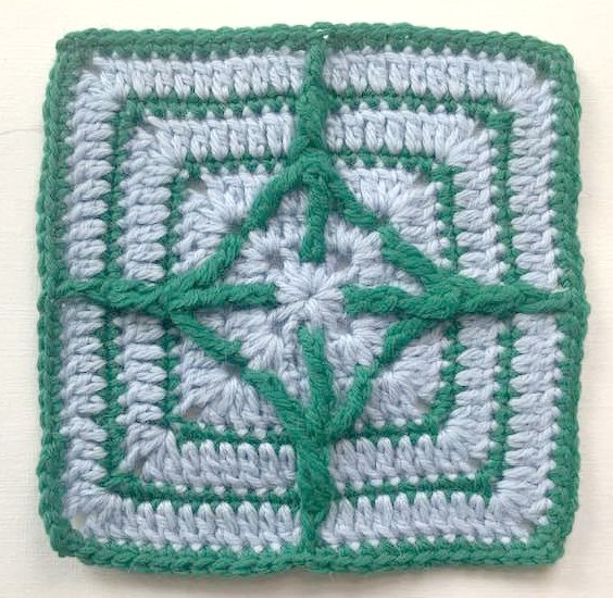 Gehäkeltes Quadrat hellblau mit grünen Linien und sternförmigem Zentrum
