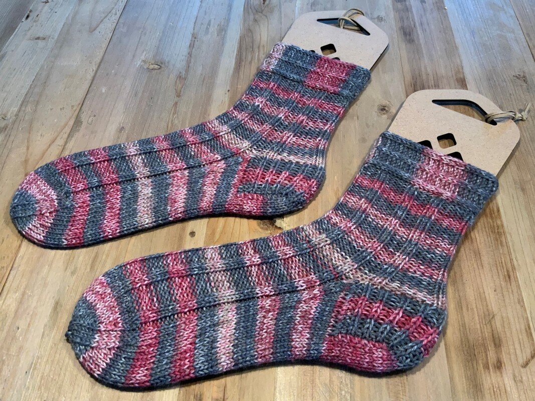 Gestricktes Paar Ringelsocken grau und rosa auf Holzsockenform liegend