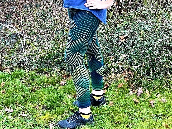 Beine in gestrickten Leggings mit grünem geometrischem Muster auf Gras