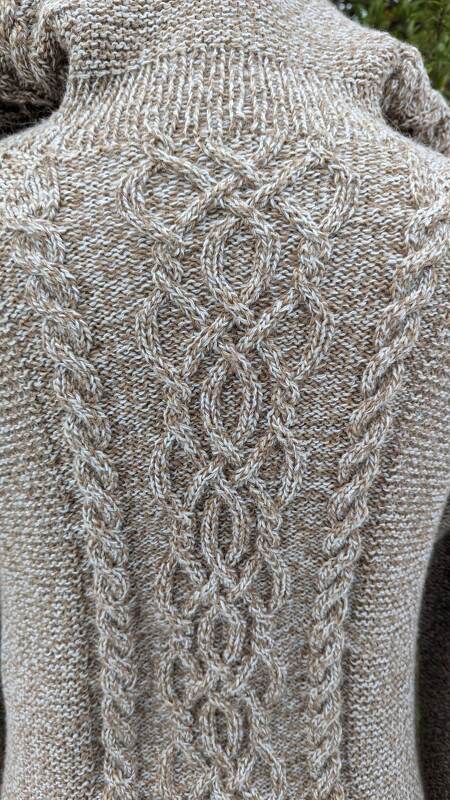 Detaillierte Rückenansicht einer braun-beigen Strickjacke mit komplexem Zopfmuster aus Rauten und vertikalen Zöpfen