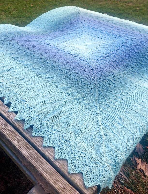 Handgehäkelte Decke mit Blau‑Lila‑Farbverlauf und gezackter Spitzenkante auf einer Holzbank