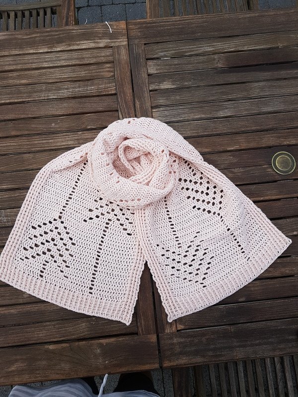 Light pink crocheted rectangular scarf with openwork leaf lace laid on a wooden table.