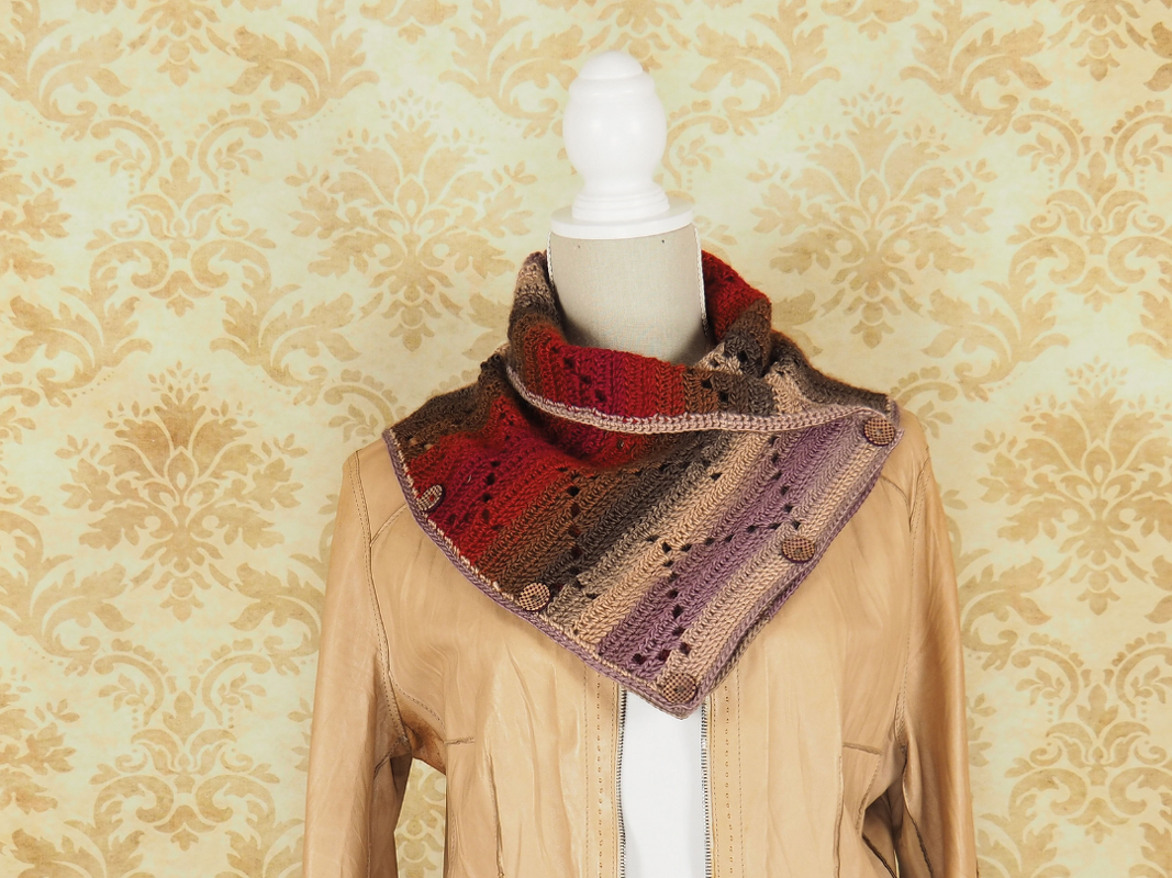 Ombre crocheted collar scarf with three buttons in red, brown, beige and purple on a mannequin wearing a beige jacket.