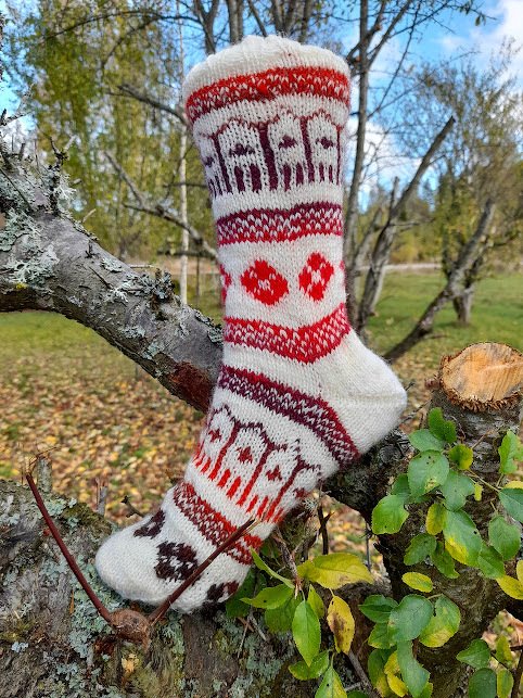 Handgestrickte cremefarbene Socke mit rot-braunem Haus- und Rautenmuster auf Ast