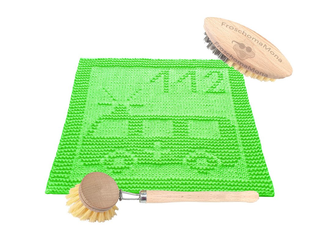 Quadratisches hellgrünes Stricktuch mit eingestricktem Krankenwagen und der Zahl 112, daneben zwei Holzbürsten.