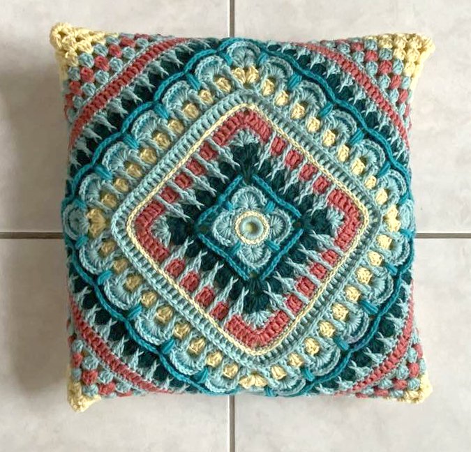 Quadratisches mehrlagiges Häkelkissen mit rosettenartiger Mitte, Muschel- und Puffstichen in Türkis, Gelb und Koralle