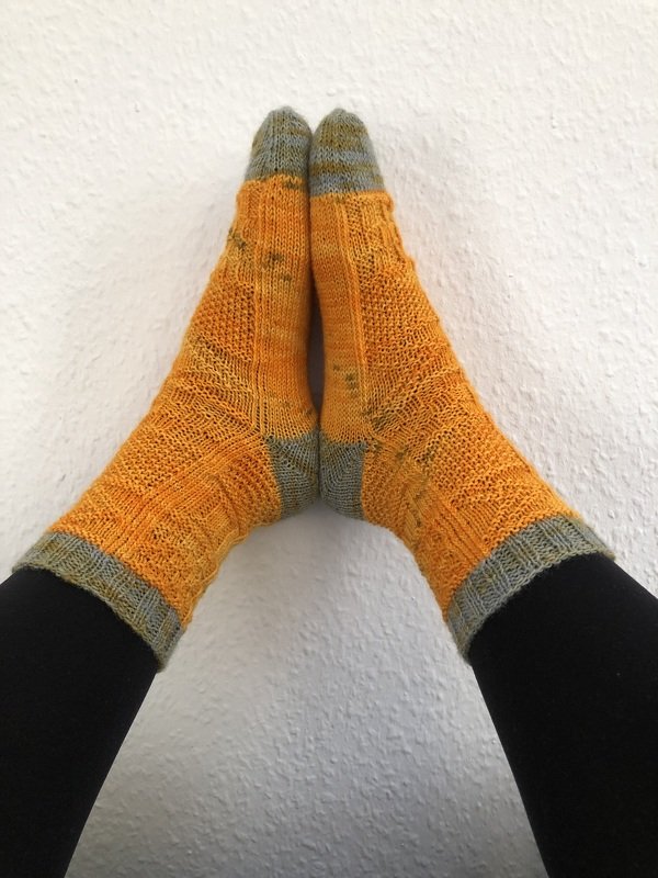 Handgestrickte orange-graue Socken an Füßen vor weißer Wand