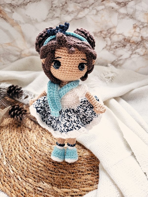 Gehäkelte Amigurumi-Puppe mit braunem Haar, hellblauem Schal und blau-weißem Kleid.