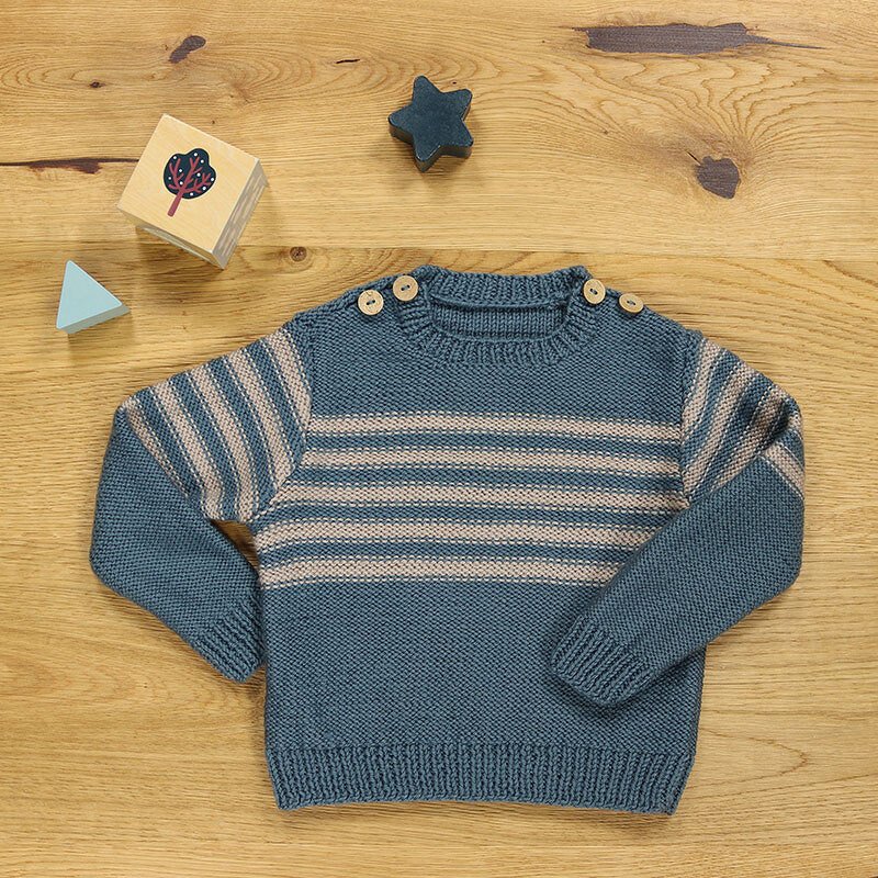 Blau-beiger gestreifter gestrickter Kinderpullover mit drei Schulterknöpfen auf Holzhintergrund
