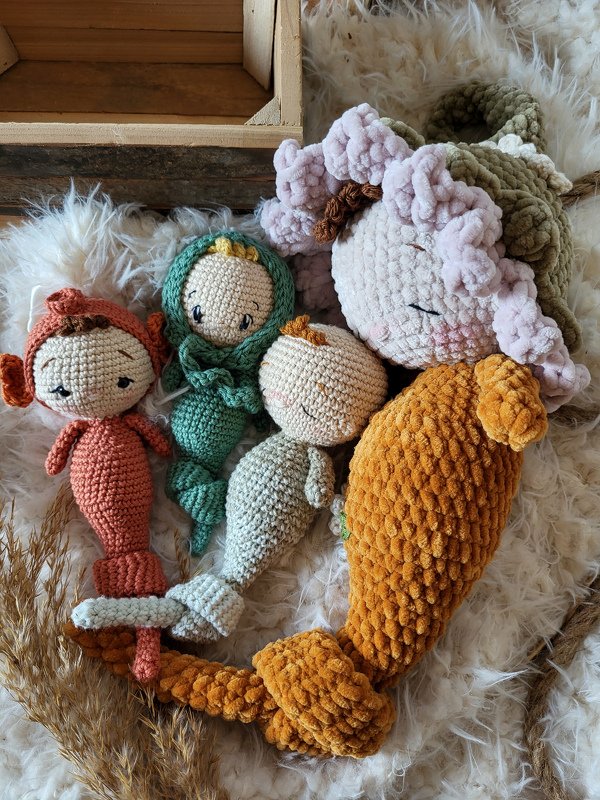 Vier gehäkelte Meerjungfrauen-Puppen in unterschiedlichen Farben und Größen auf hellem, flauschigem Untergrund