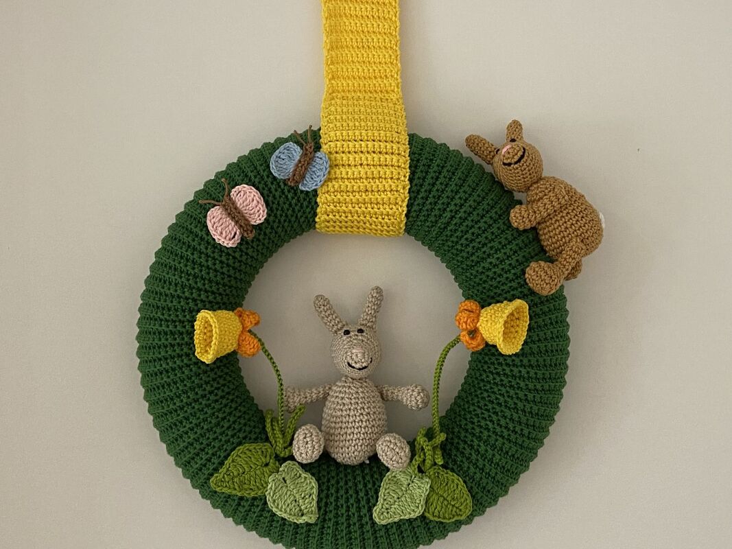 Grüner gehäkelter Oster-Türkranz mit gelbem Band, zwei Hasenfiguren, Schmetterlingen und gelben Blüten