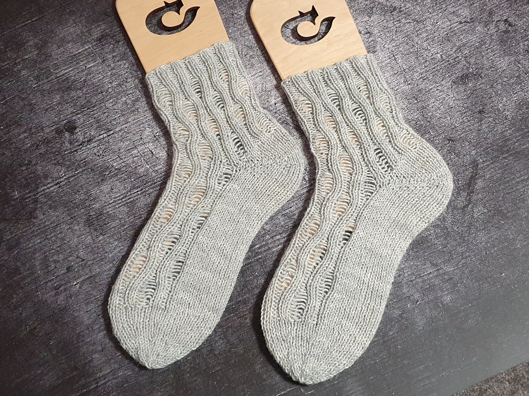 Paar hellgraue gestrickte Socken mit Ajour-Lochmuster auf Holzspannern auf dunkelgrauem Untergrund