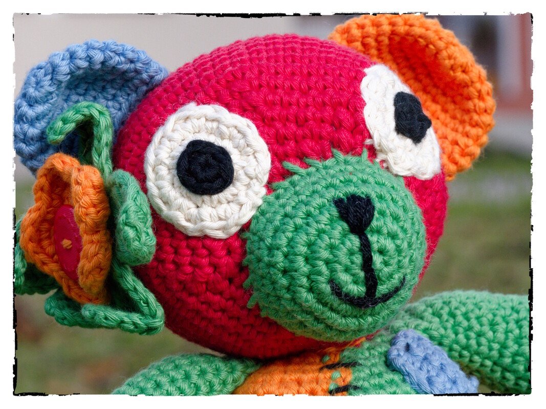 Nahaufnahme eines bunten gehäkelten Amigurumi-Teddybären mit rotem Kopf, grüner Schnauze und bunten Ohren.