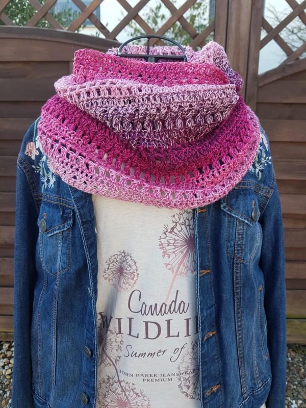 Mehrfarbiger gehäkelter Loopschal in Pinktönen auf einer Schaufensterpuppe über einer Jeansjacke