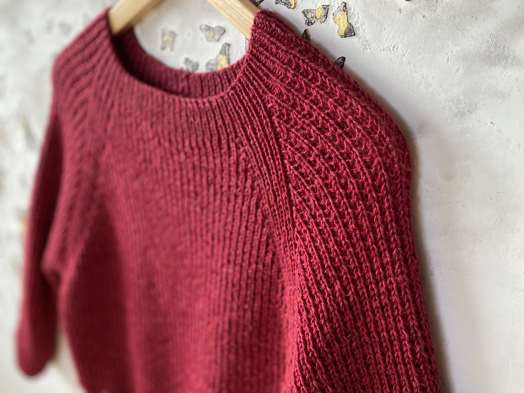 Dark red knitted women's sweater with boat neckline and lace raglan sleeves on a wooden hanger.