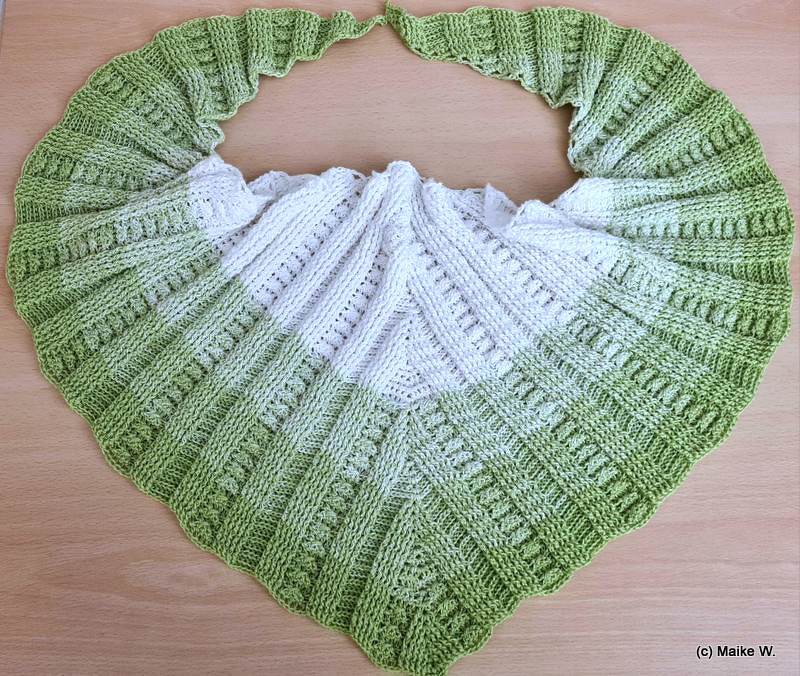 Gehäkeltes Dreieckstuch in Weiß und Hellgrün mit Rippen- und Lochmustern, flach auf einer Holzoberfläche ausgelegt.