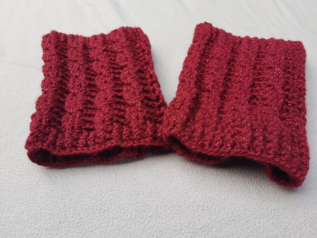Paar burgunderrote gehäkelte Beinstulpen mit Rippmuster auf hellem Stoff