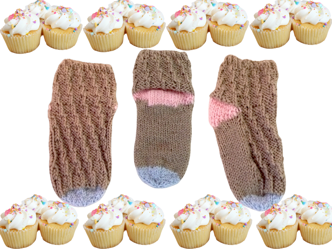 Drei gestrickte Babysocken braun mit rosa und hellblauen Akzenten, dekorative Cupcakes am Rand