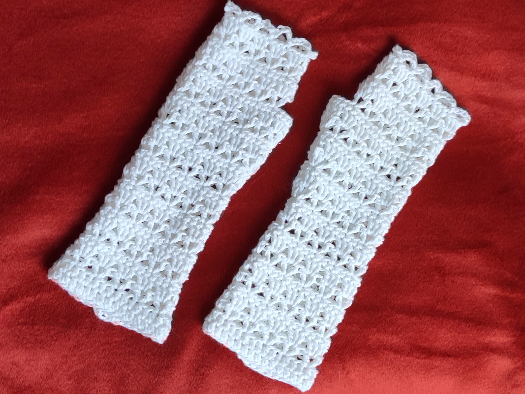 Zwei weiße fingerlose Armstulpen mit Häkel-Lochmuster auf rotem Stoff